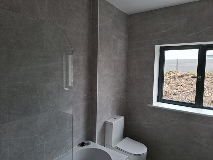 Full-height marble-effect wall tiling with a curved bath screen and tiled window reveal