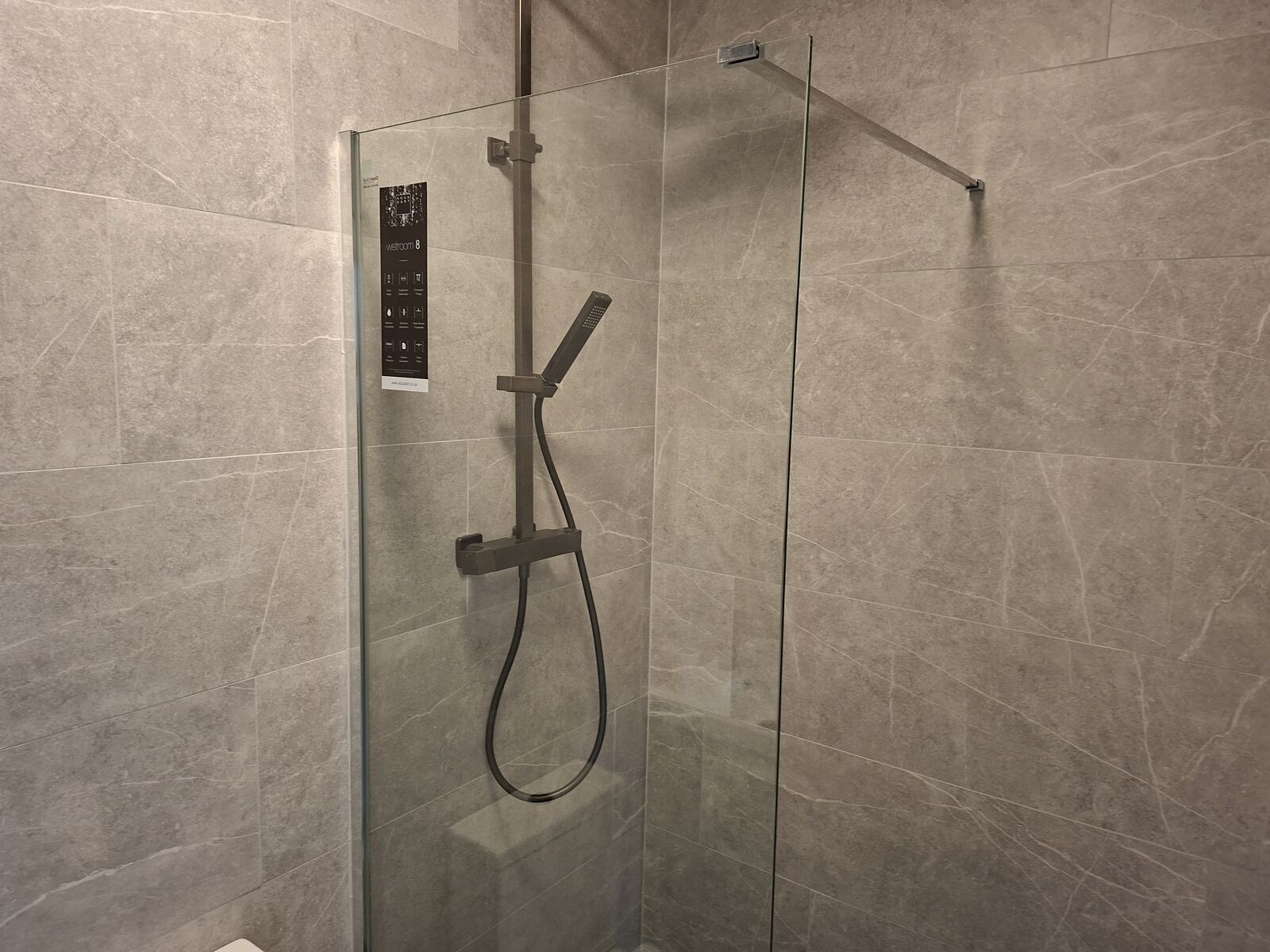 Walk-in shower with frameless glass panel and marble-effect wall tiles